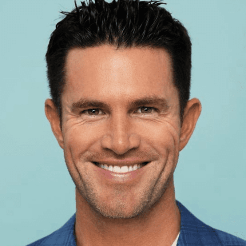 A man with dark hair smiling against a plain background.