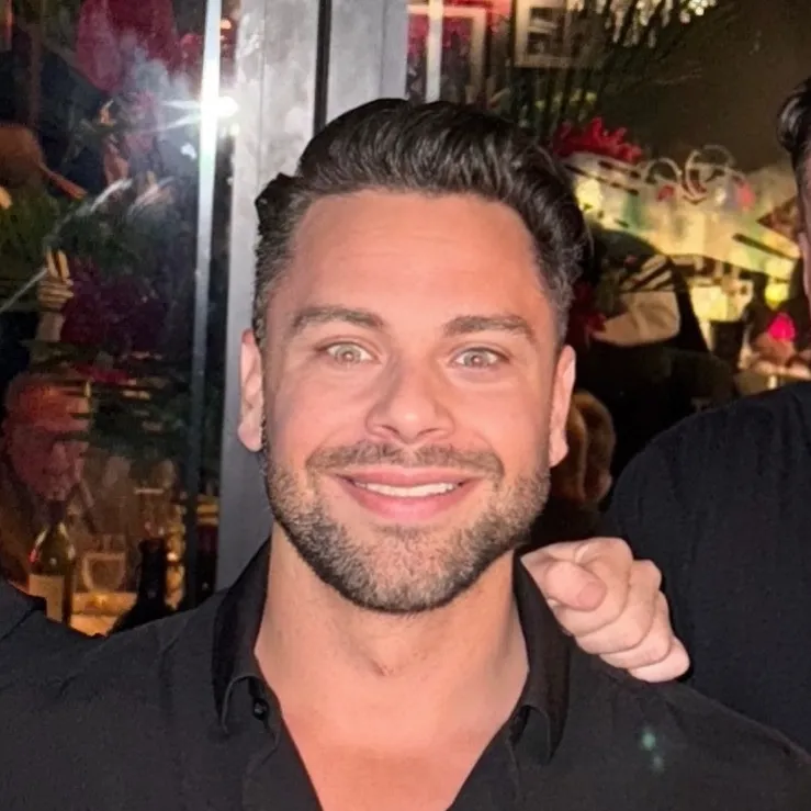 A smiling man with a beard in a lively nighttime setting.