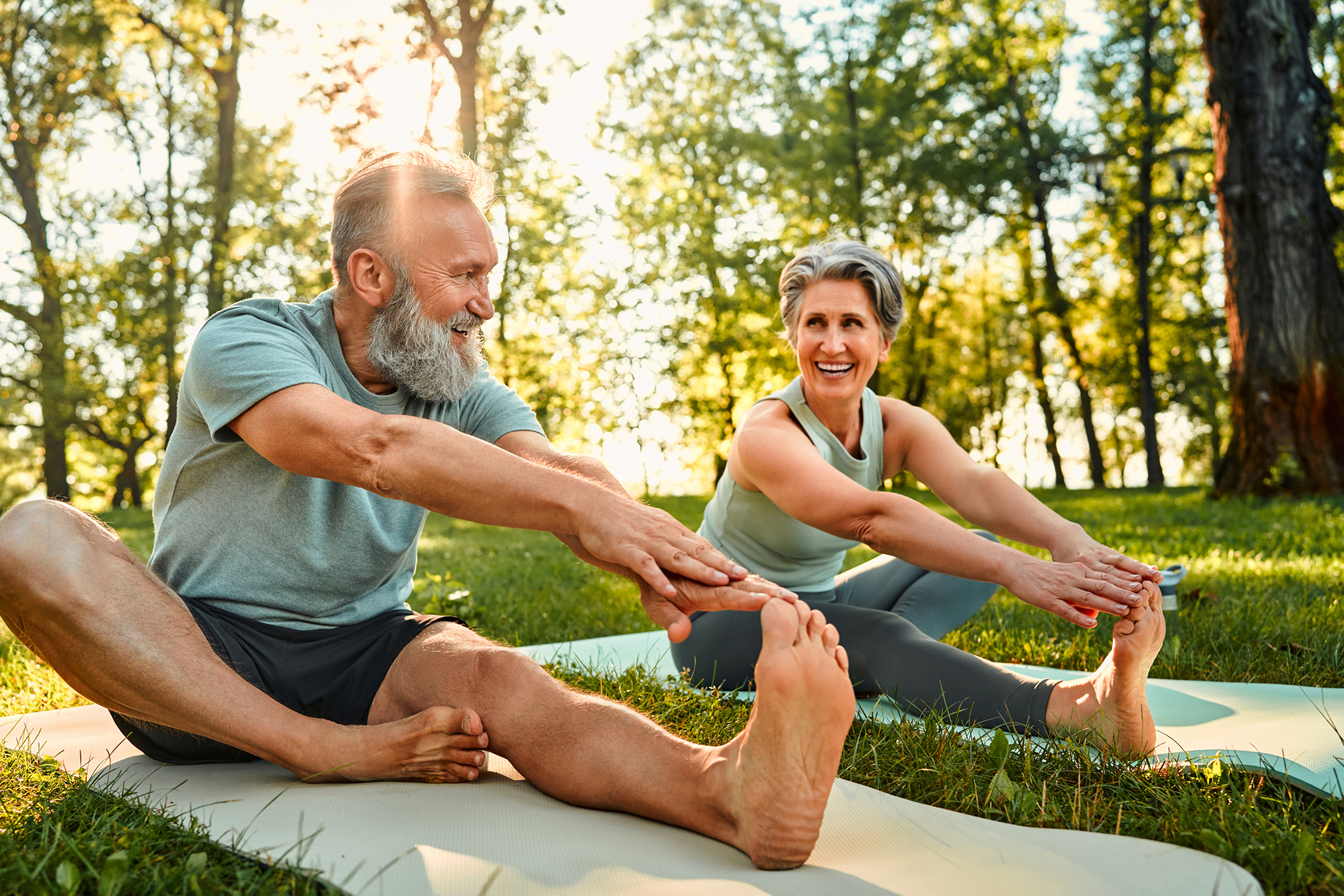 Older couple stretching outdoors on yoga mats.