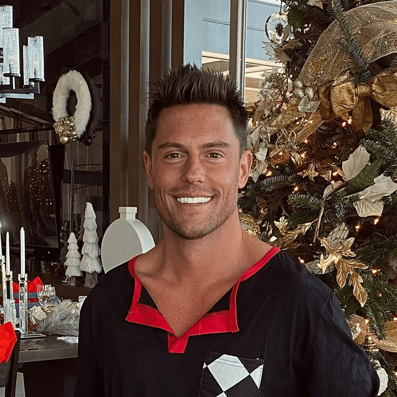 Smiling man in a black and red shirt standing indoors near festive decor.