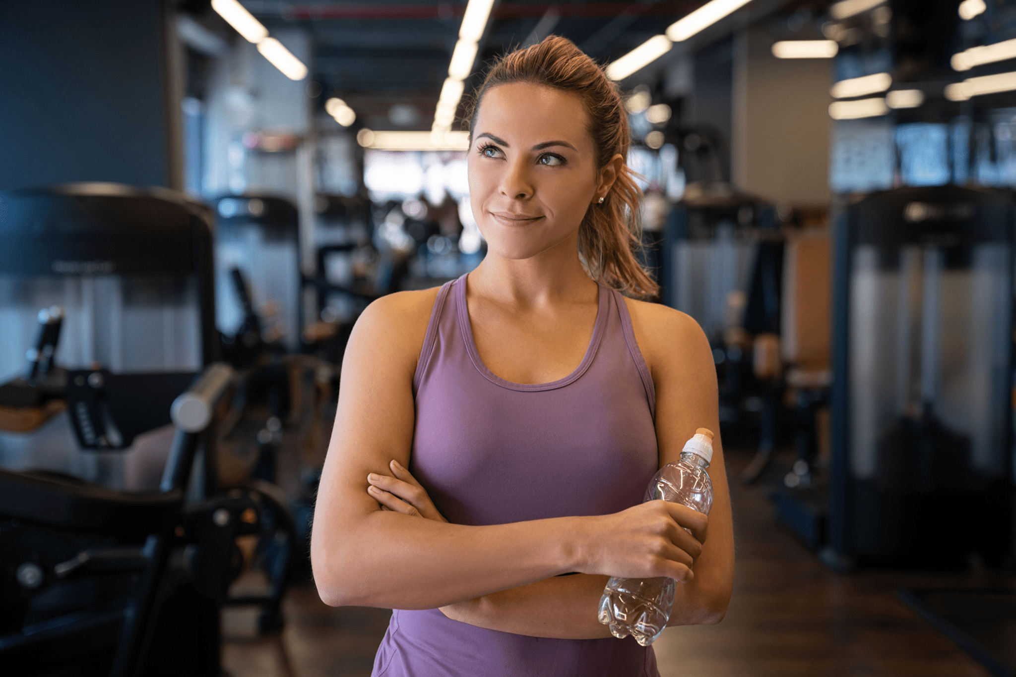 Woman in gym holding water bottle, looking focused.
