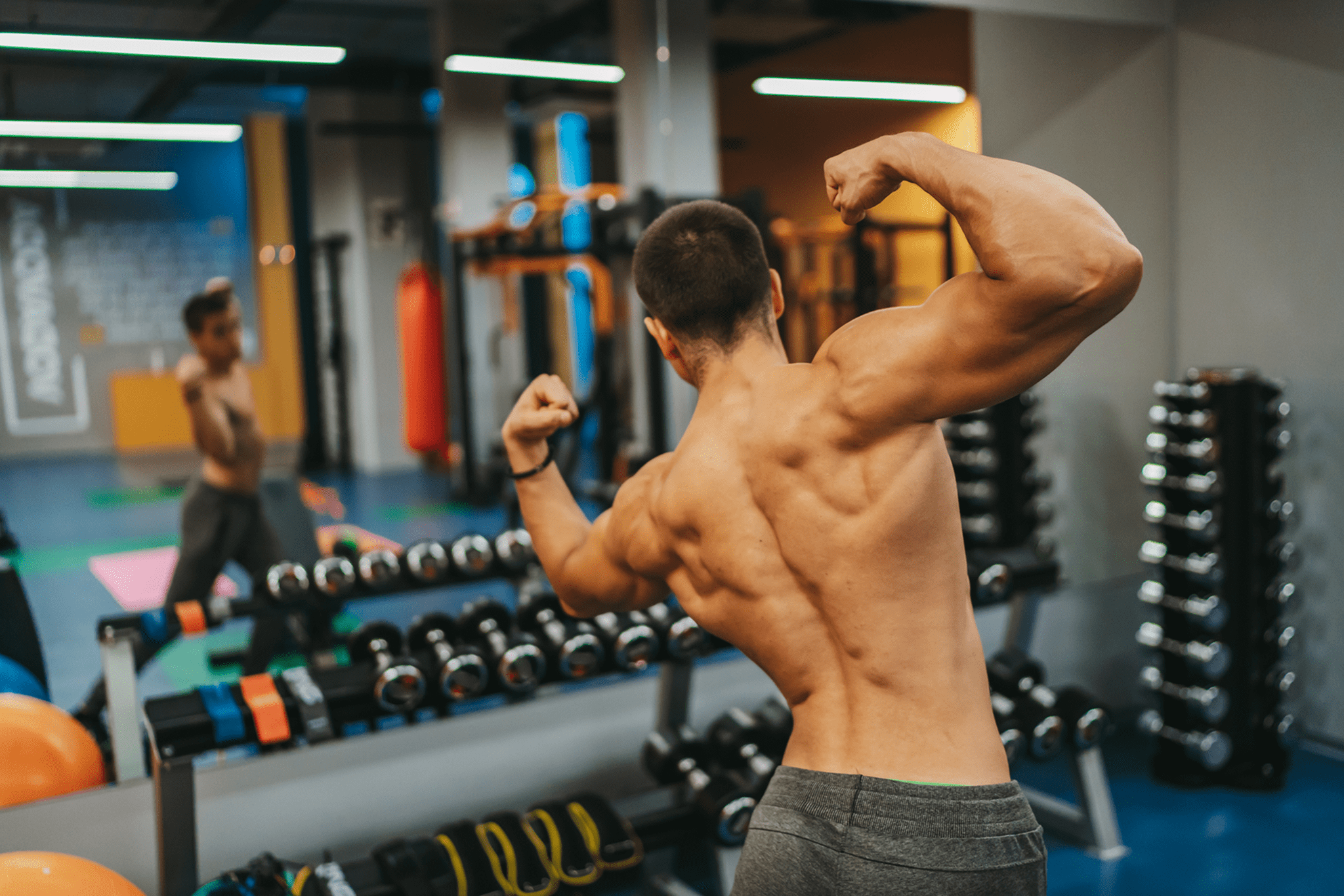 Muscular man flexing back muscles in gym mirror.