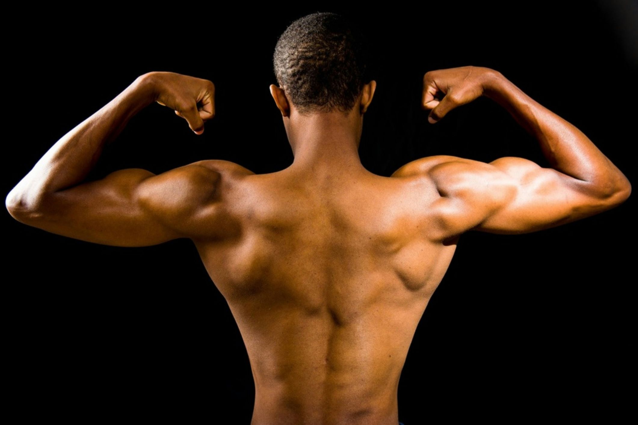 Man flexing muscular back and arms against black background.
